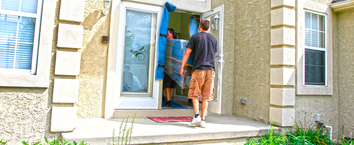 movers carrying a large piece of furniture, which has been blanket wrapped for protection