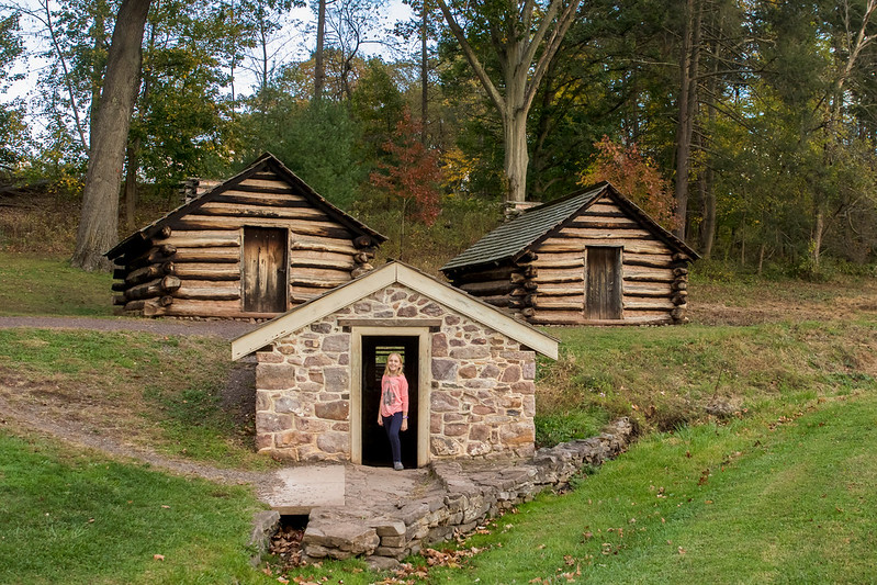 a girl in a pink shirt stands in front of an old, small stone building 