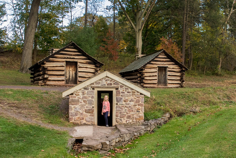 a girl in a pink shirt stands in front of an old, small stone building