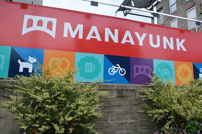 A sign that says "Manayunk" and has icons for a pretzel, beer, bike and bridge